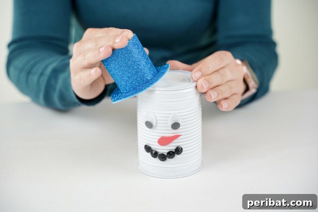 DIY Painted Tin Can Snowman Video Tutorial 23 Attaching the blue top hat at a slight angle onto the top of the tin can head, securing it with glue.