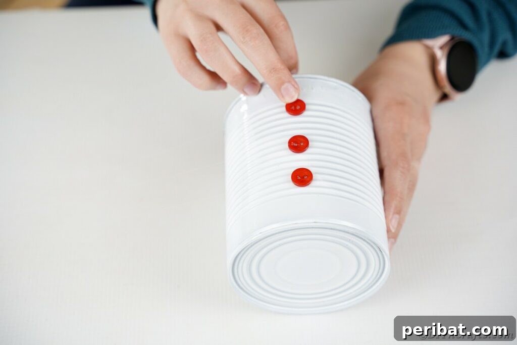 DIY Painted Tin Can Snowman Video Tutorial 24 Gluing three red buttons in a vertical line down the center of the larger tin can, forming the snowman's body.