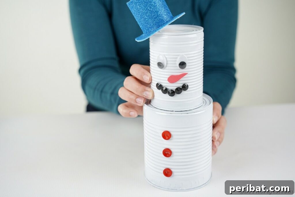 DIY Painted Tin Can Snowman Video Tutorial 25 The smaller tin can (head) being securely glued onto the larger tin can (body), forming the complete snowman structure.