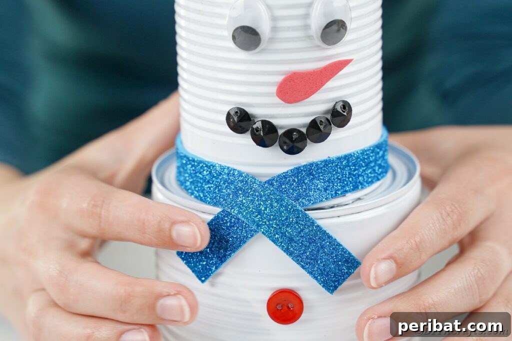 DIY Painted Tin Can Snowman Video Tutorial 26 A person holding a finished tin can snowman, proudly displaying its charming details including the foam paper scarf.