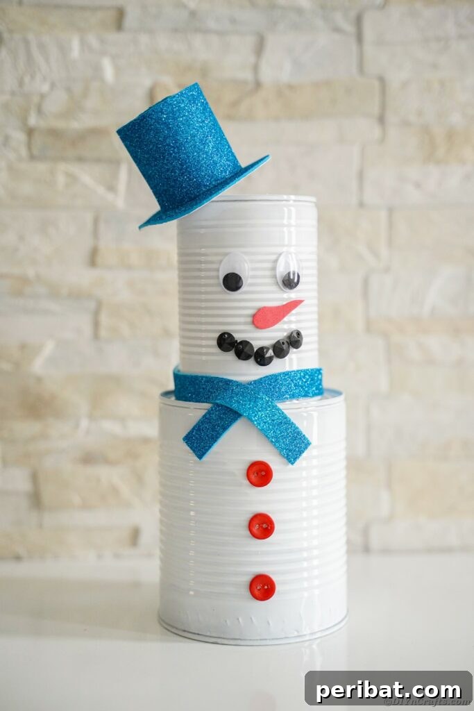 DIY Painted Tin Can Snowman Video Tutorial 27 A finished tin can snowman decoration, complete with hat, scarf, and buttons, displayed against a brick wall.