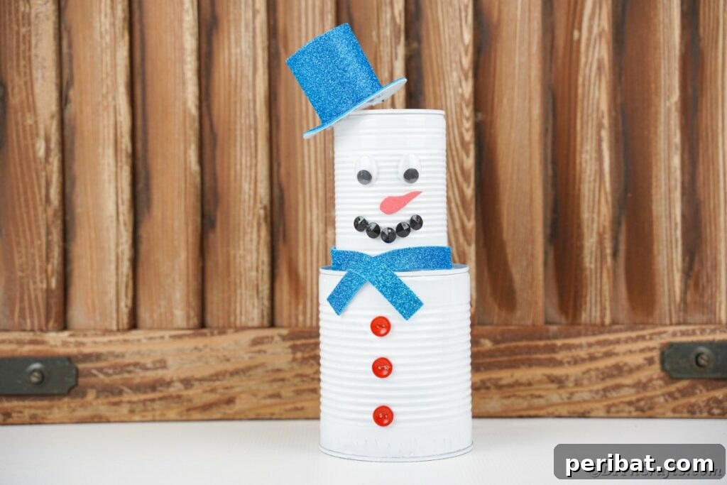DIY Painted Tin Can Snowman Video Tutorial 6 A completed tin can snowman decoration displayed elegantly against a warm wooden wall, ready for winter.