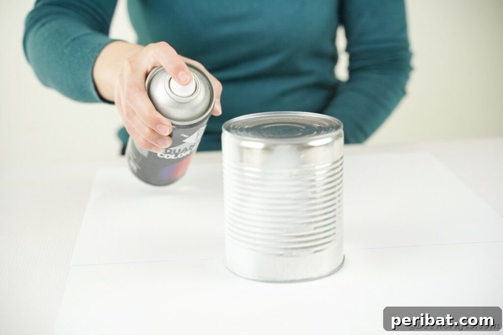 DIY Painted Tin Can Snowman Video Tutorial 8 Someone carefully applying white spray paint to tin cans, preparing them for the snowman craft project.