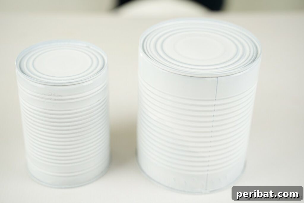 DIY Painted Tin Can Snowman Video Tutorial 9 Several tin cans, freshly painted white, resting on a surface and drying completely before the next steps of the craft.