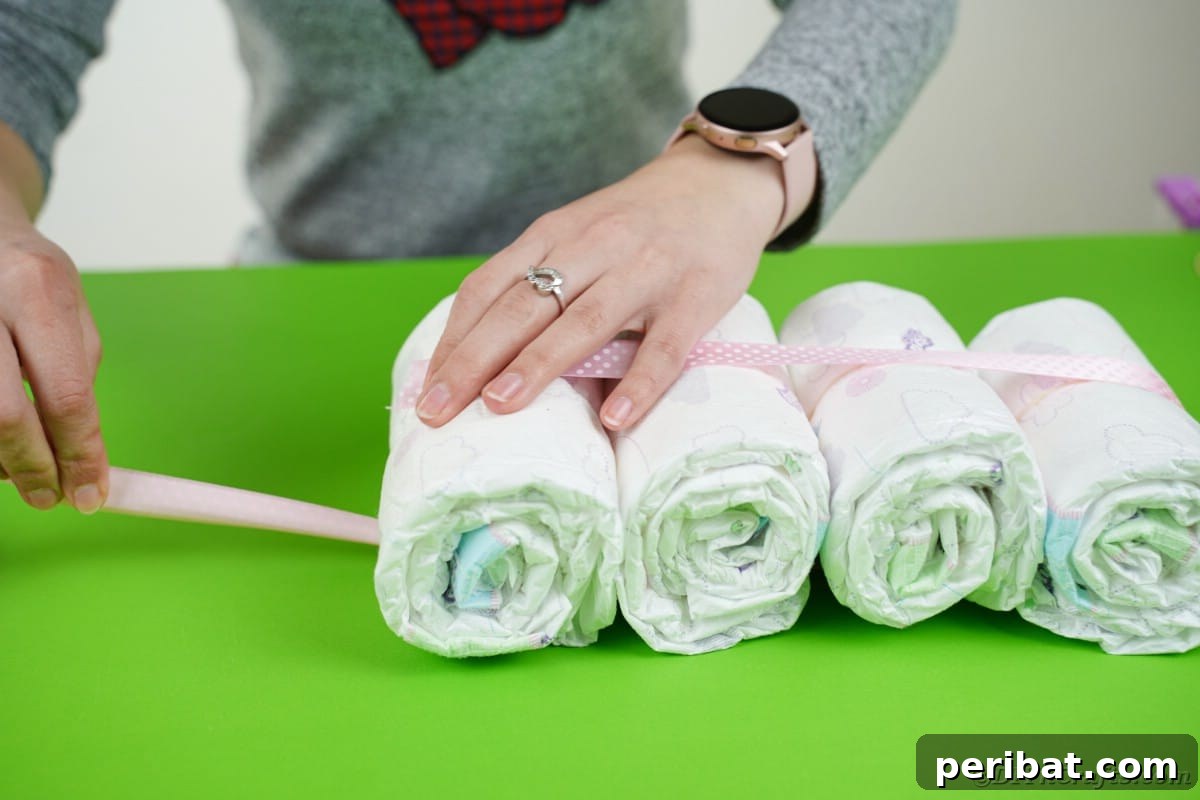 Create a Charming Diaper Train for Baby Shower Joy 11 Ribbon being carefully wrapped around a set of bundled diapers, creating the first carriage of the diaper cake train.
