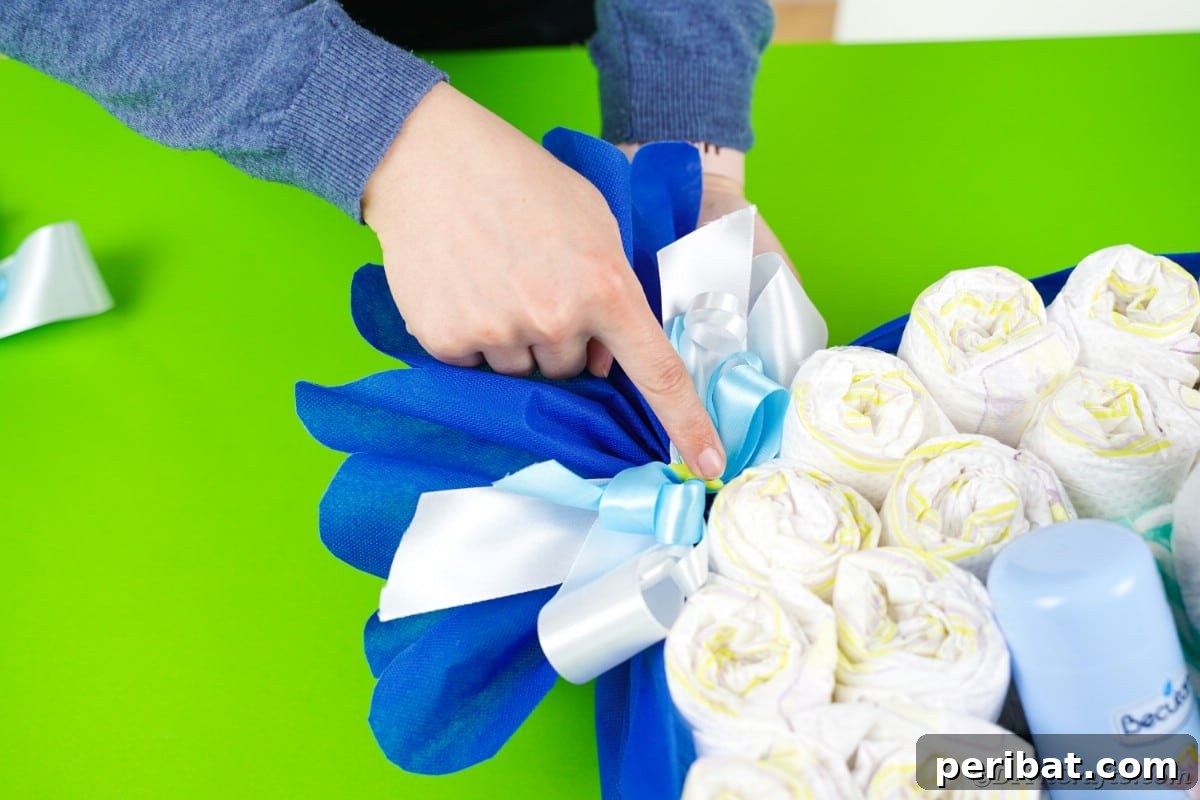 Adding a decorative bow to the cinched side of the candy wrapper diaper cake, enhancing its gift-like appearance.