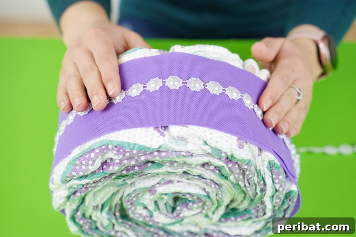 Decorative beaded ribbon being carefully glued around the center of the purple diaper cake, enhancing its aesthetic appeal.
