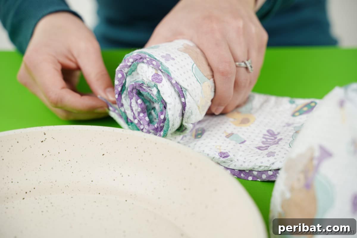 A close-up image showing a single diaper being carefully rolled, preparing it for inclusion in the snail diaper cake structure.