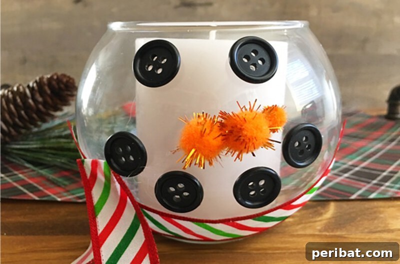 A charming snowman candle holder made from an inverted clear glass bowl, decorated with a painted snowman face and a small fabric scarf, holding a tealight candle.