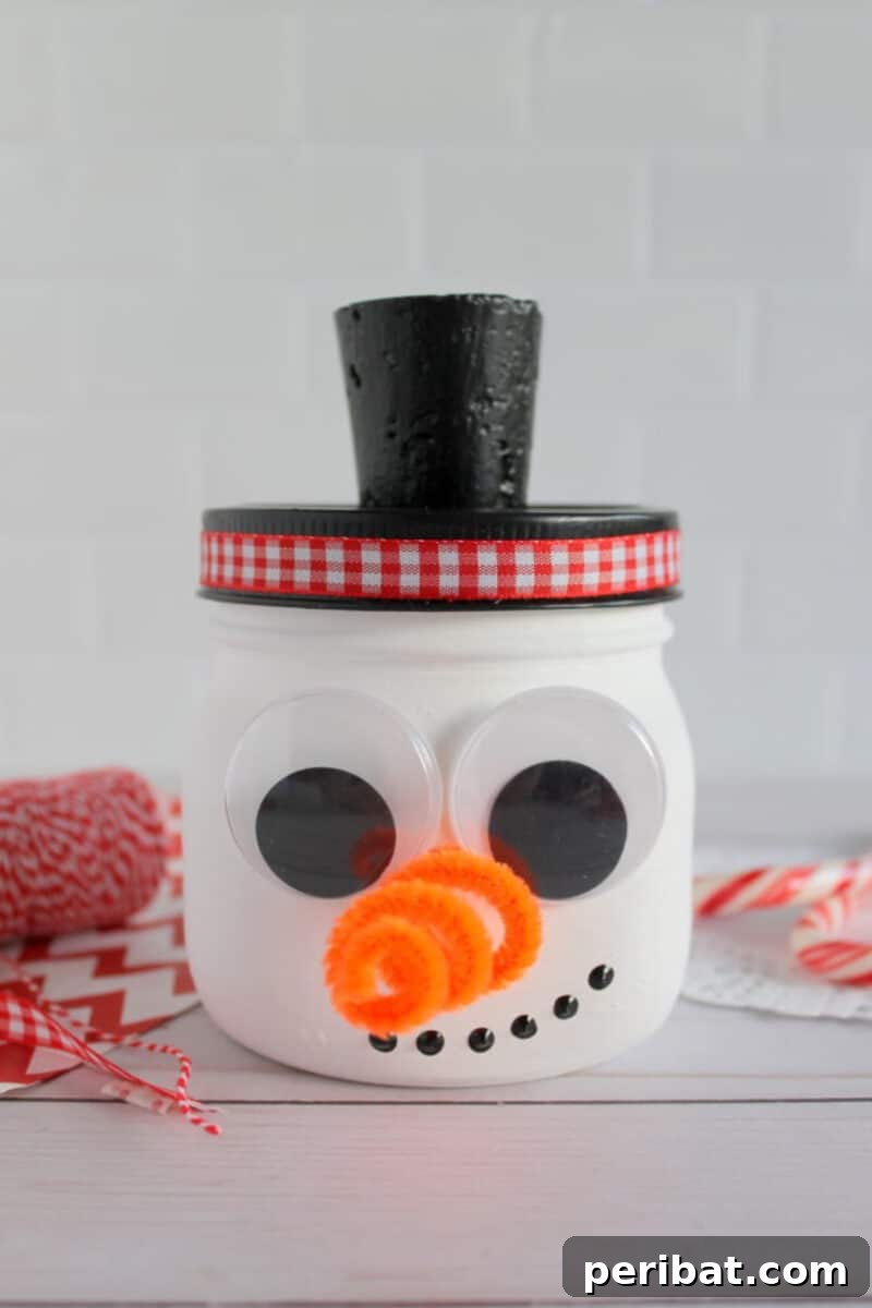 A cheerful Mason jar snowman, painted white and decorated with a friendly face, buttons, and a small scarf, standing on a kitchen counter.