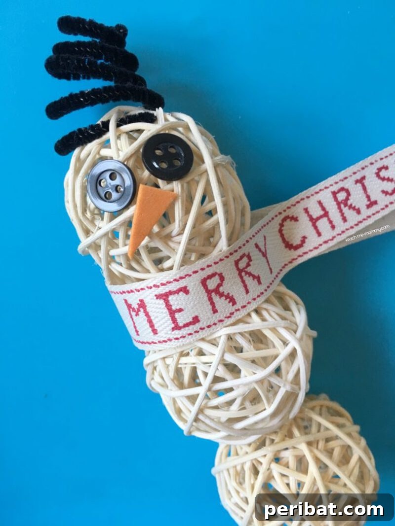 A rustic snowman ornament made from a painted round wood slice with a fabric scarf, pinecone hat, and twig arms, set on a blue surface.