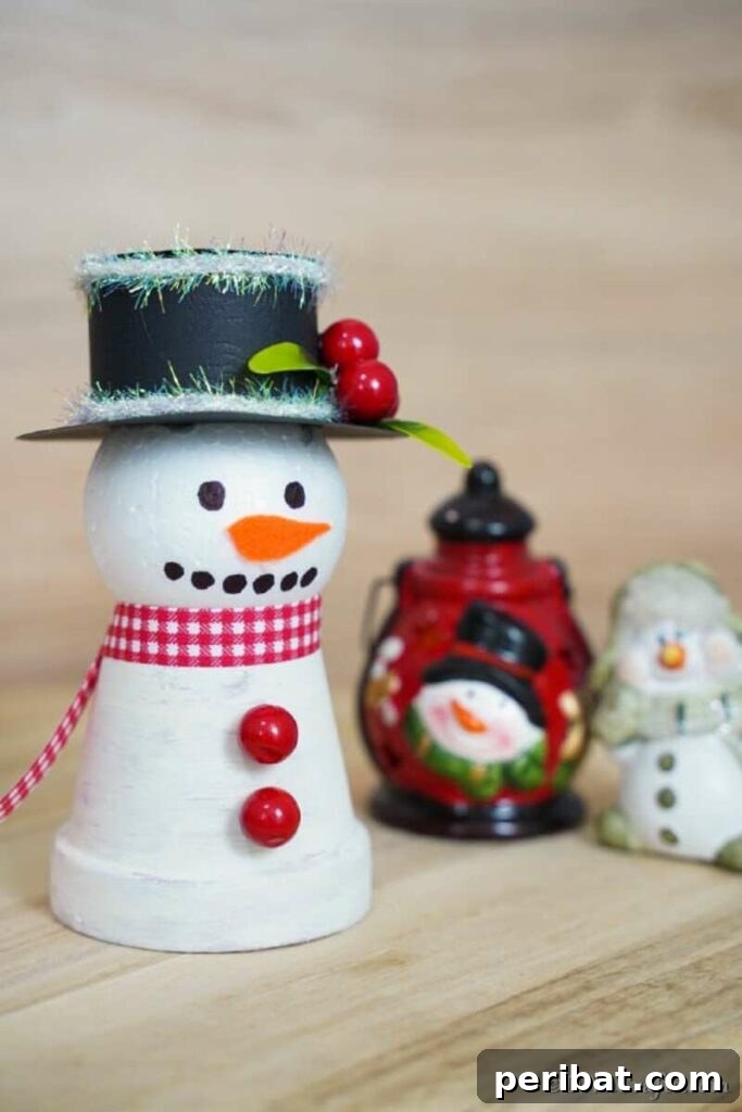 A festive clay pot snowman decoration, painted white and adorned with winter details, sitting on a wooden table, perfect for holiday home decor.