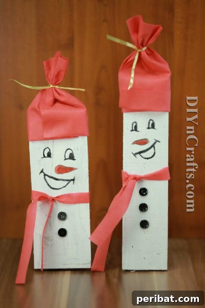 A rustic snowman decoration made from stacked pieces of scrap wood, painted white and decorated with fabric and buttons, standing against a snowy background.
