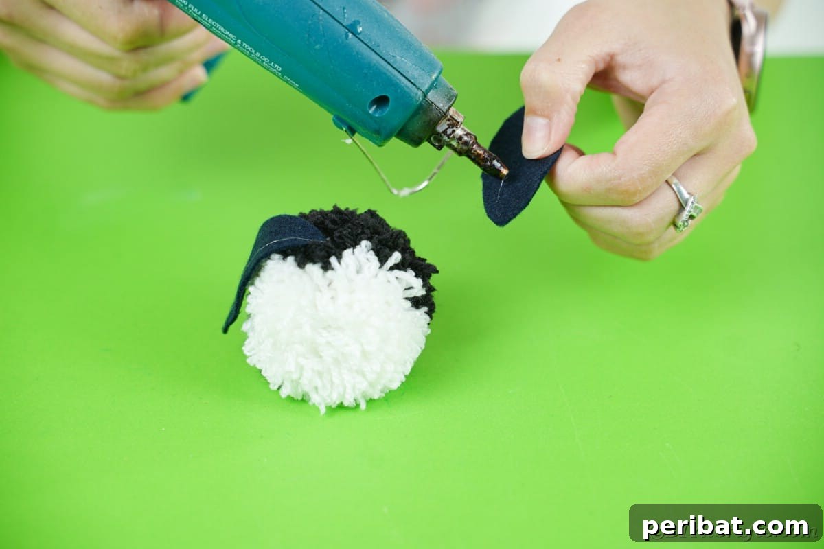 Handmade Pom Pom Penguin Winter Charm 16 Gluing felt wings onto a pom pom for the penguin's body
