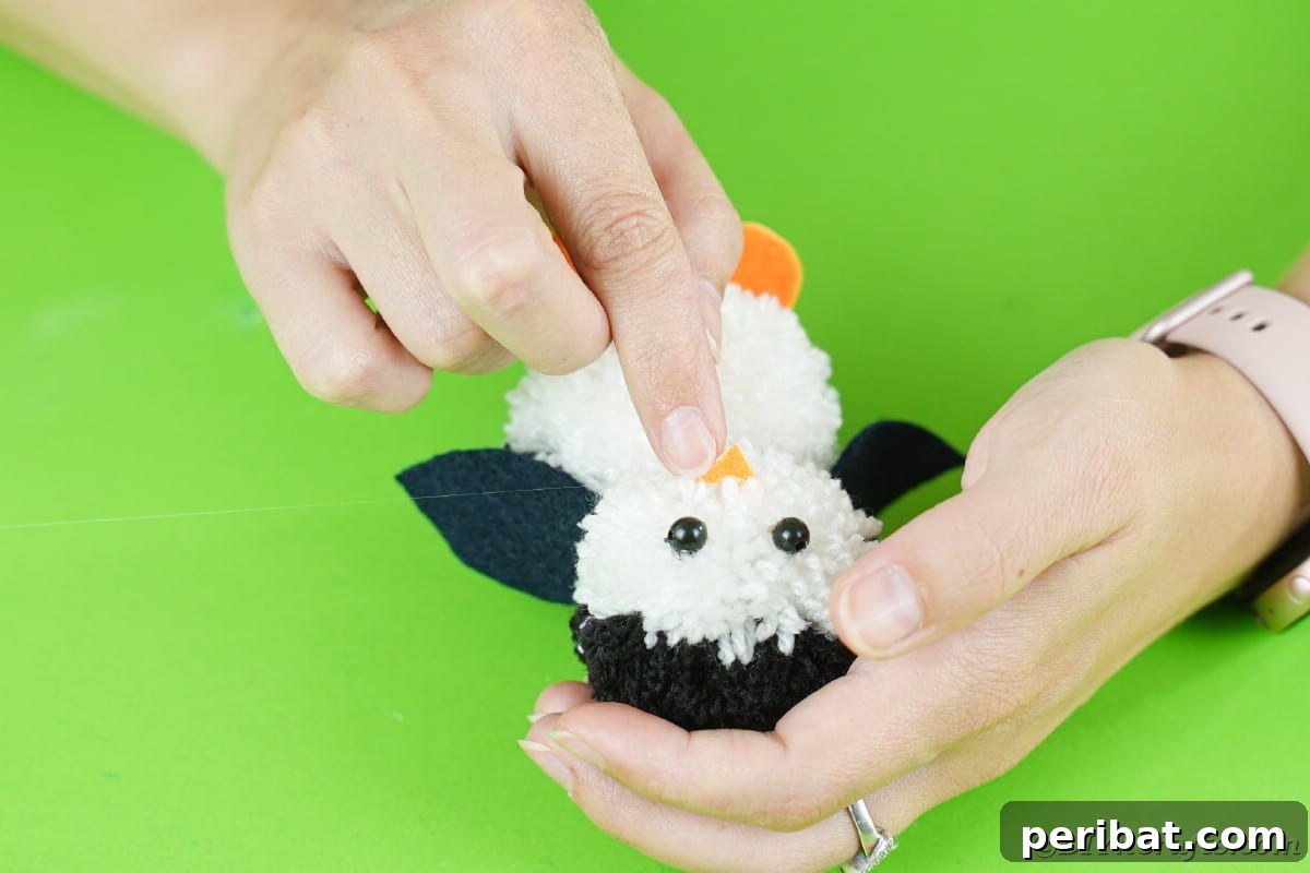 Handmade Pom Pom Penguin Winter Charm 20 Gluing an orange foam paper beak onto the pom pom penguin