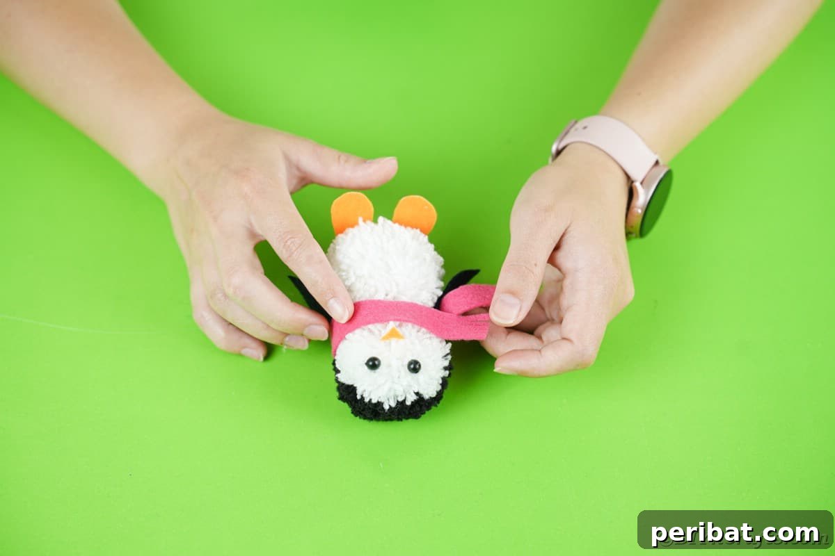 Handmade Pom Pom Penguin Winter Charm 21 Gluing a felt scarf around the neck of the pom pom penguin
