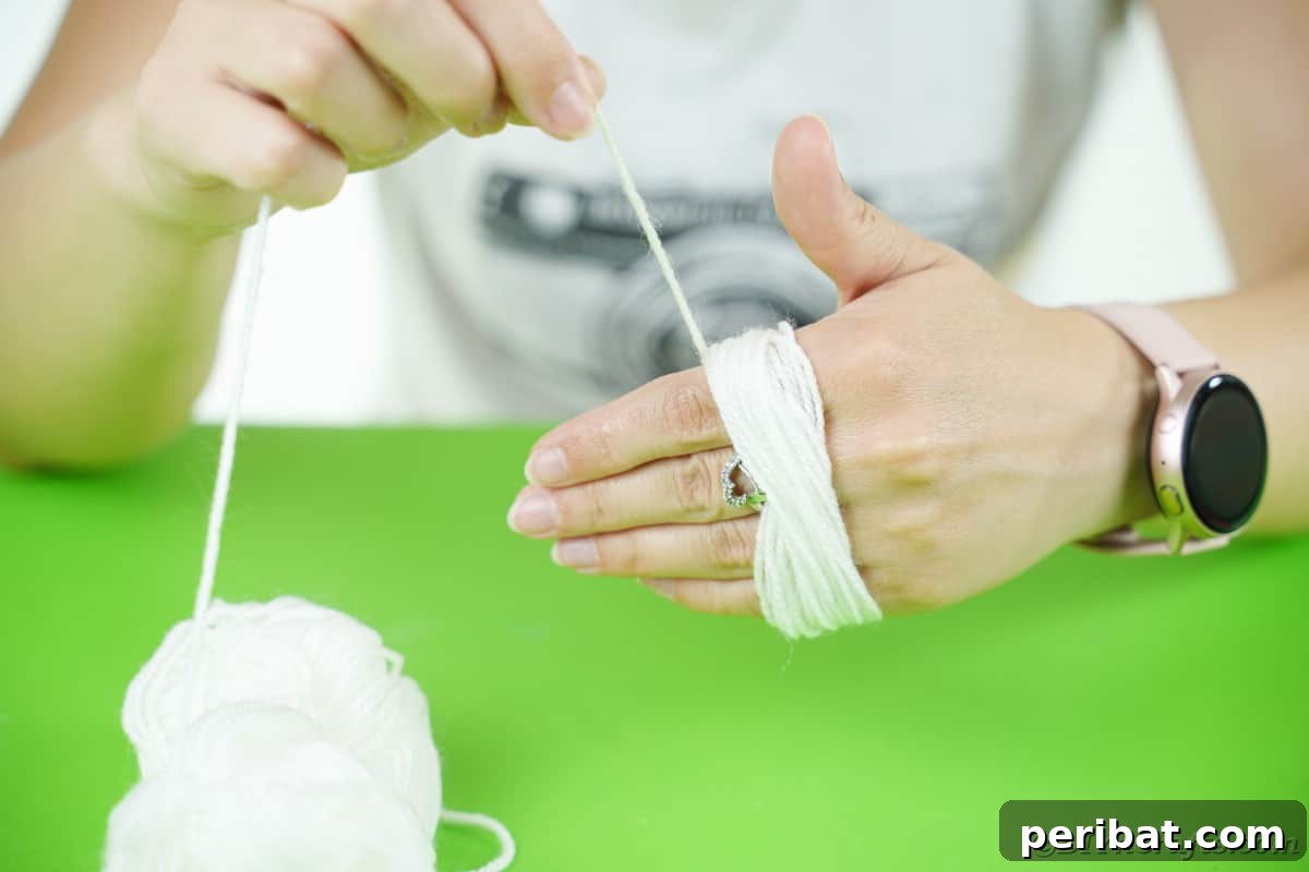 Handmade Pom Pom Penguin Winter Charm 9 White yarn being wrapped around a hand to form a pom pom