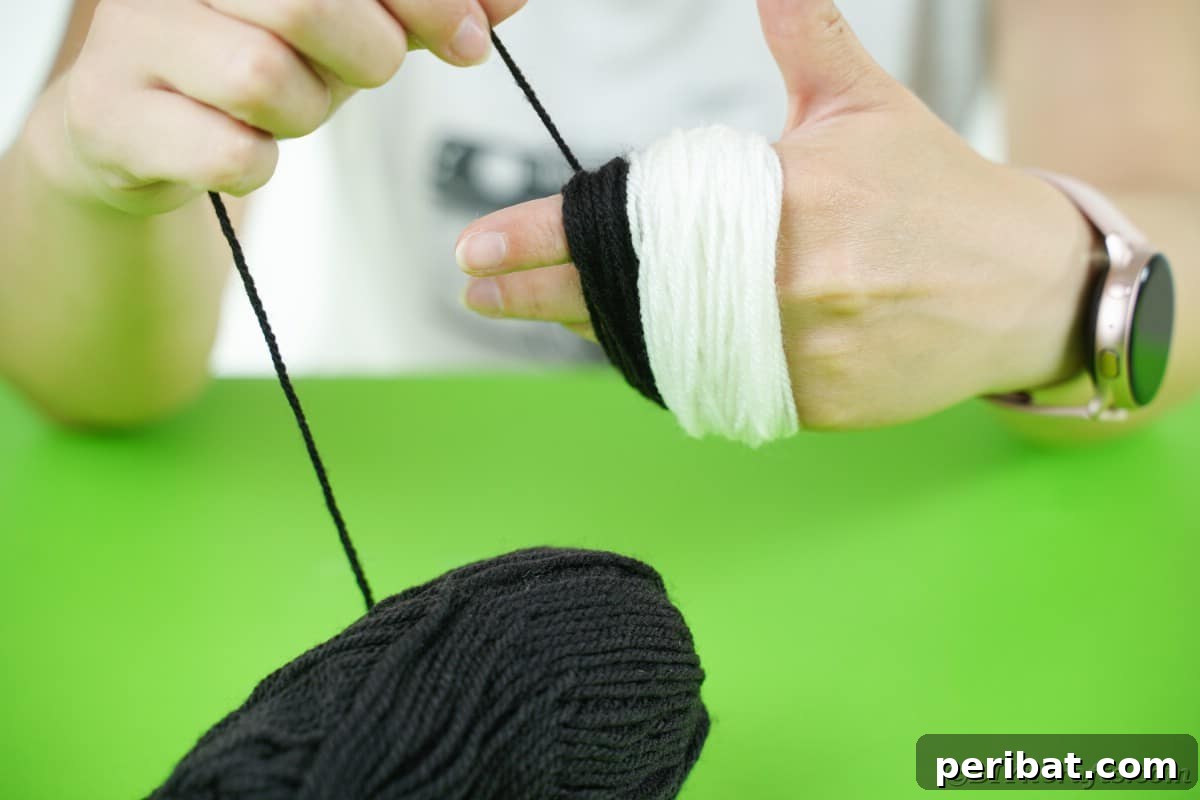 Handmade Pom Pom Penguin Winter Charm 10 Black yarn being wrapped over white yarn on a hand for a two-toned pom pom