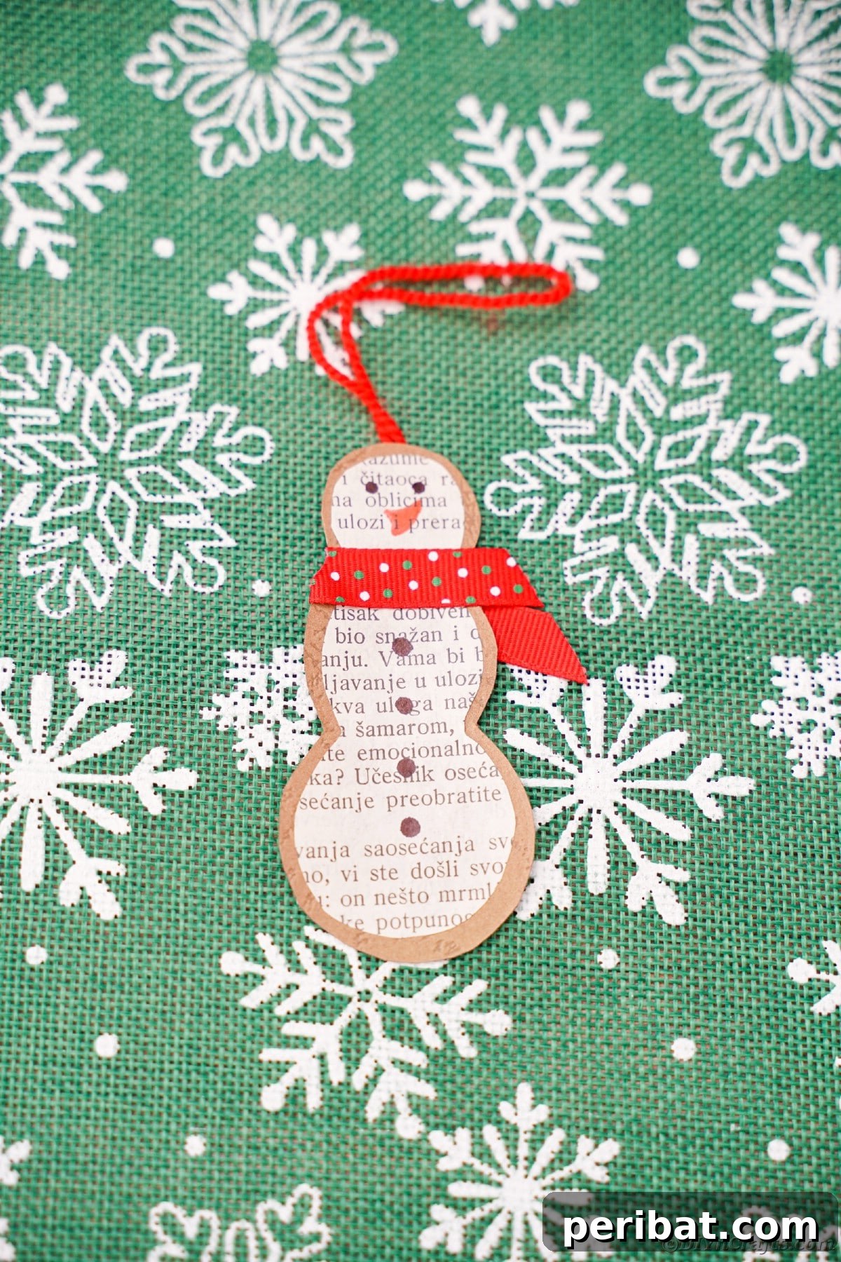 Vintage Book Page Snowman Ornament 18 Close-up of a paper snowman ornament on green craft paper