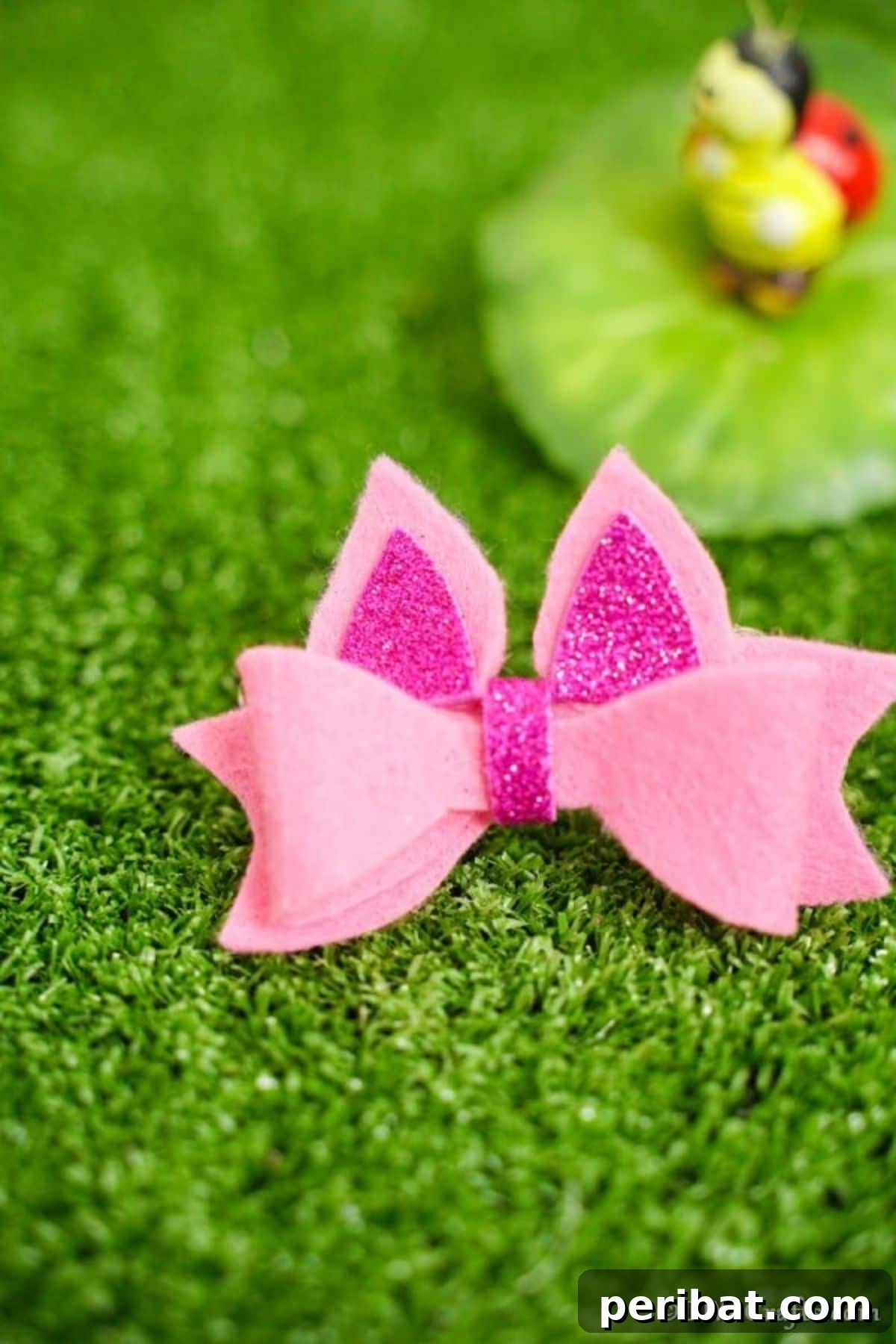 A delicate pink no-sew felt hair bow resting on grass, a sweet and simple DIY accessory that can be customized with various colors and embellishments.
