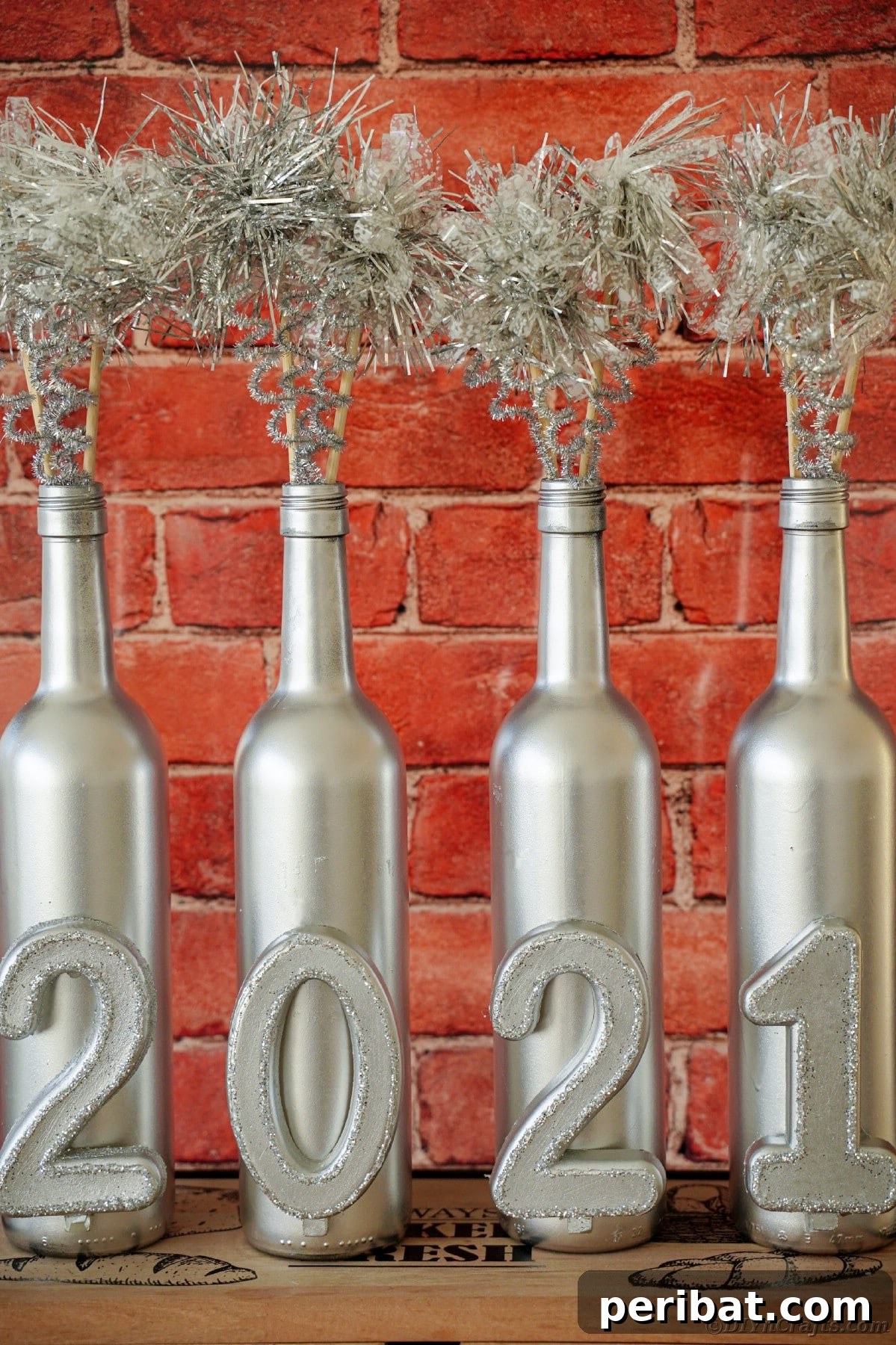 Close-up of three silver-painted wine bottles with New Year's numbers against a rustic red brick background, part of a table display.