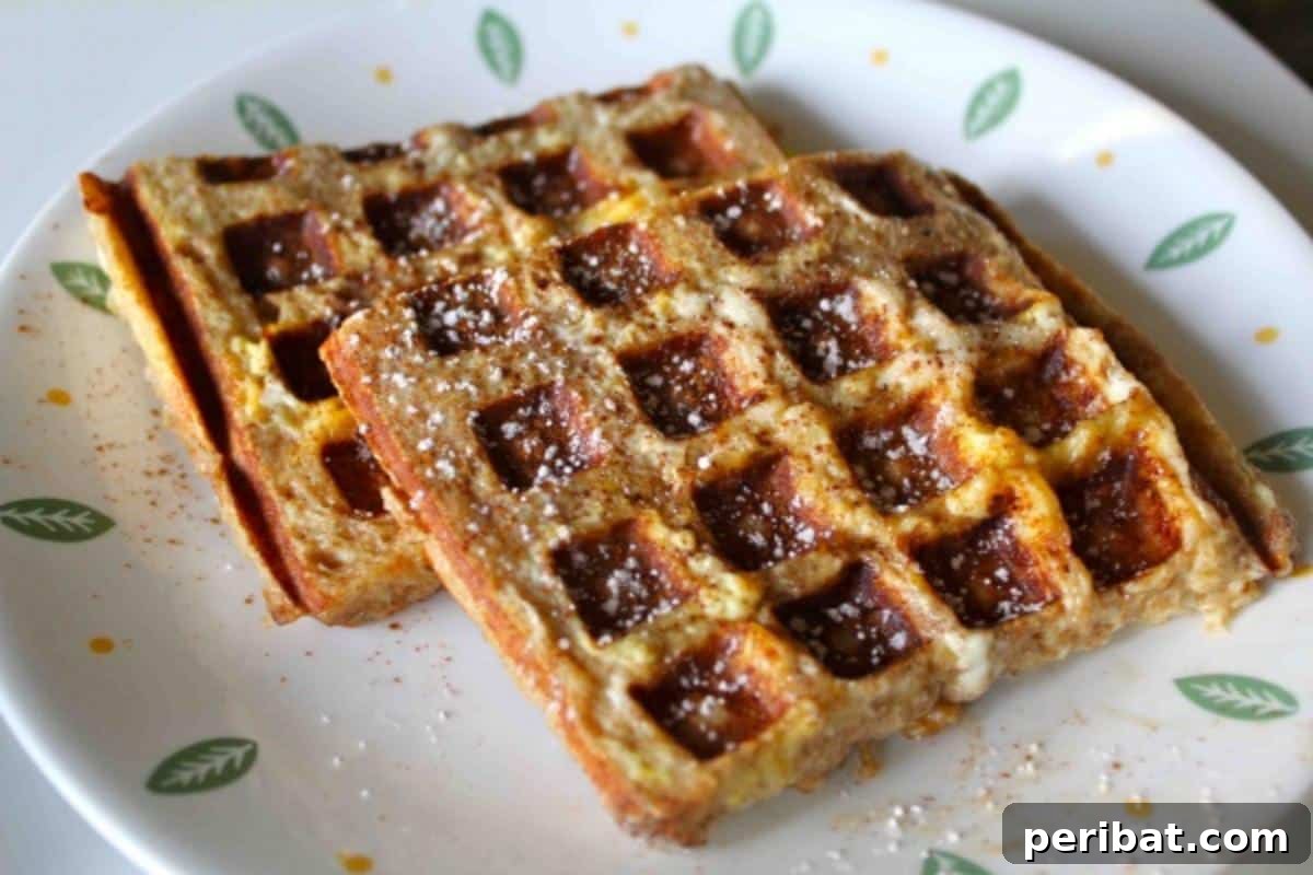 Thick slices of French toast cooked in a waffle iron, creating a unique texture and golden-brown finish, drizzled with maple syrup.