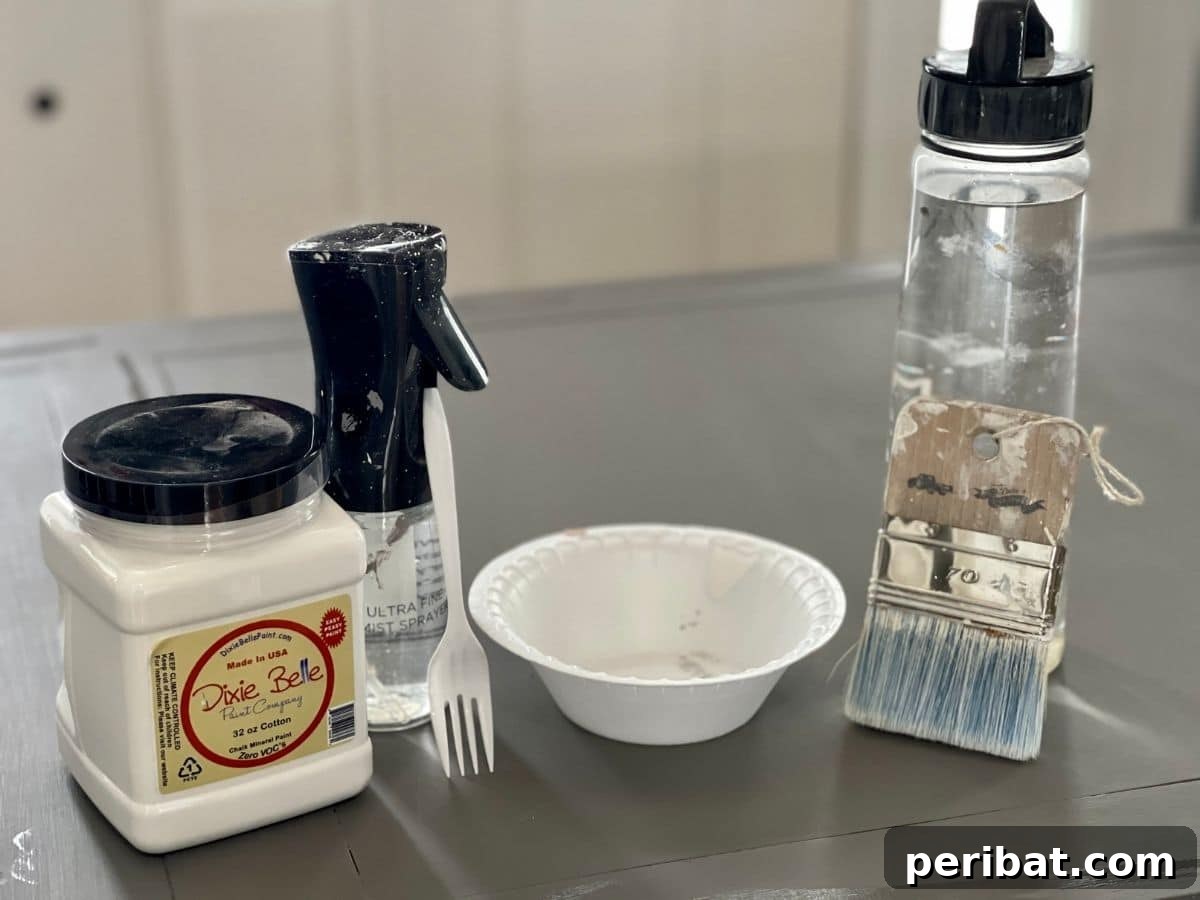 Supplies for whitewashing, including Dixie Belle Cotton paint and water, laid out on a desk surface.