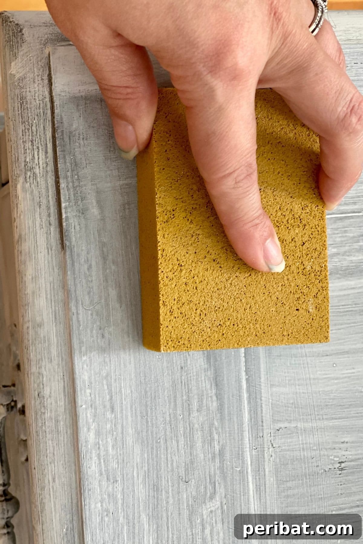 Sanding the surface of a distressed desk to reveal underlying paint layers and achieve a weathered look.