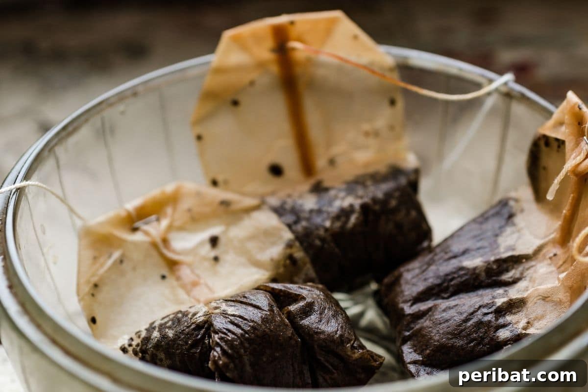 13 Clever Tea Bag Uses for a Healthier Garden 16 Three used tea bags resting in a clear glass bowl, ready for repurposing.