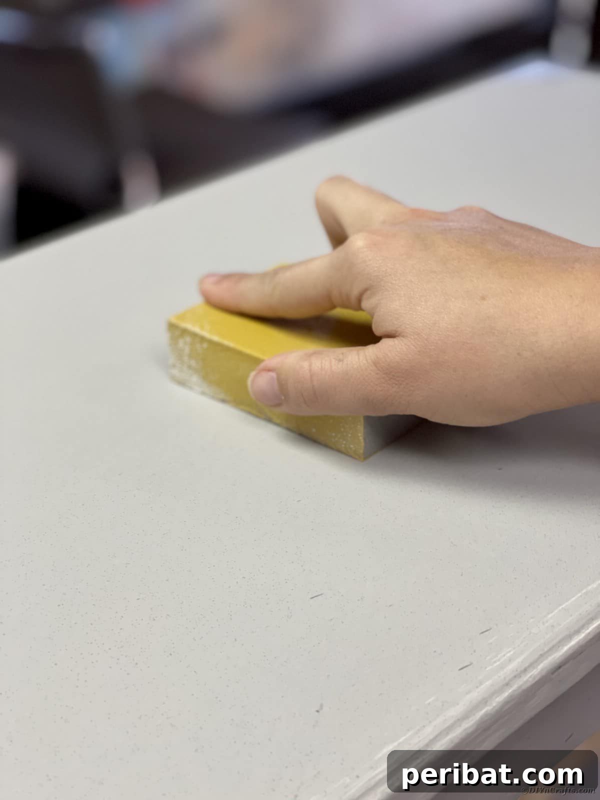 Lightly sanding a painted furniture piece with 220-grit sandpaper to smooth drips