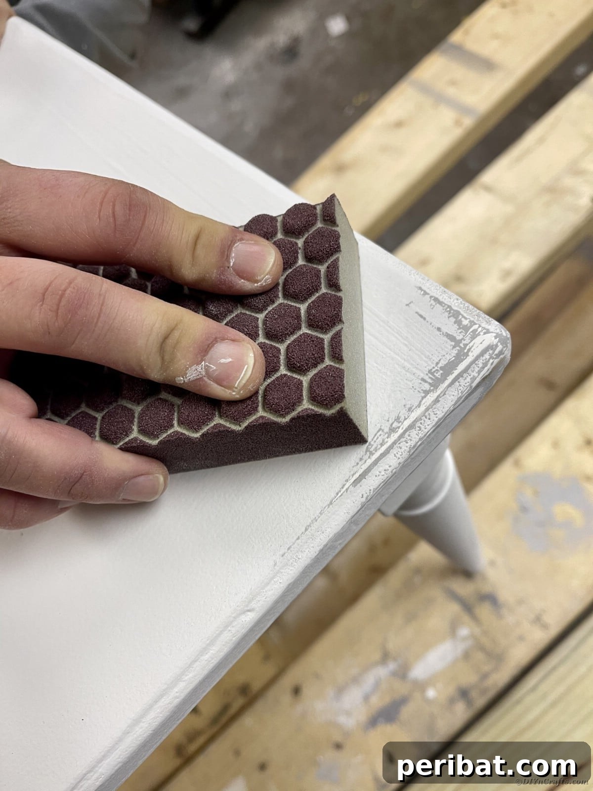Sanding a painted bench with 220-grit sandpaper to reveal the distressed base coat
