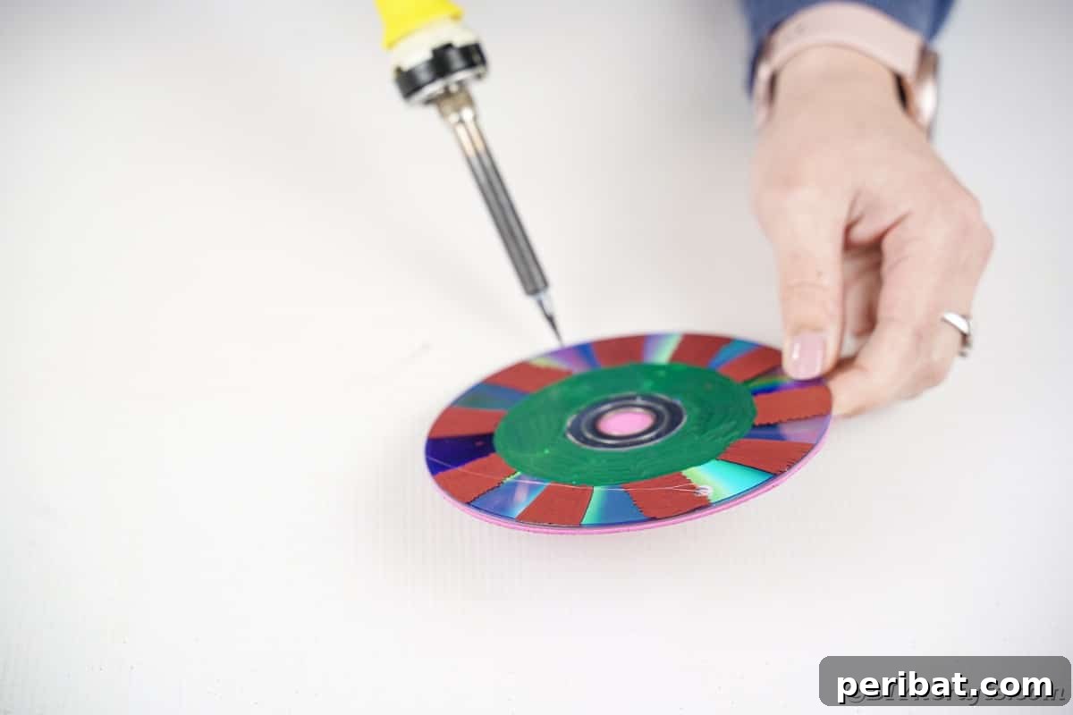 Sparkling Repurposed Garden Melody 13 A person using a soldering iron to create a small, precise hole in the edge of a decorated CD.
