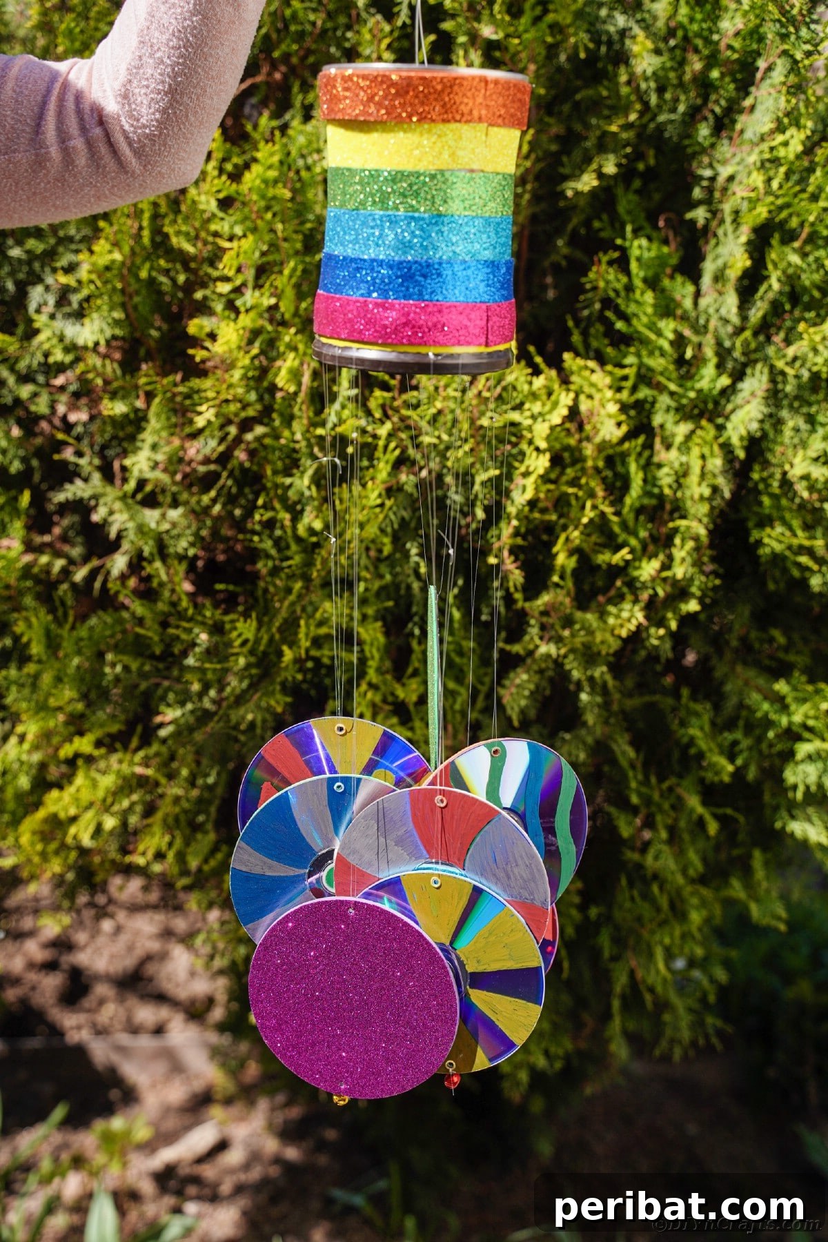 Sparkling Repurposed Garden Melody 22 A woman holding a vibrant, homemade wind chime by a green bush, showing off the finished craft.