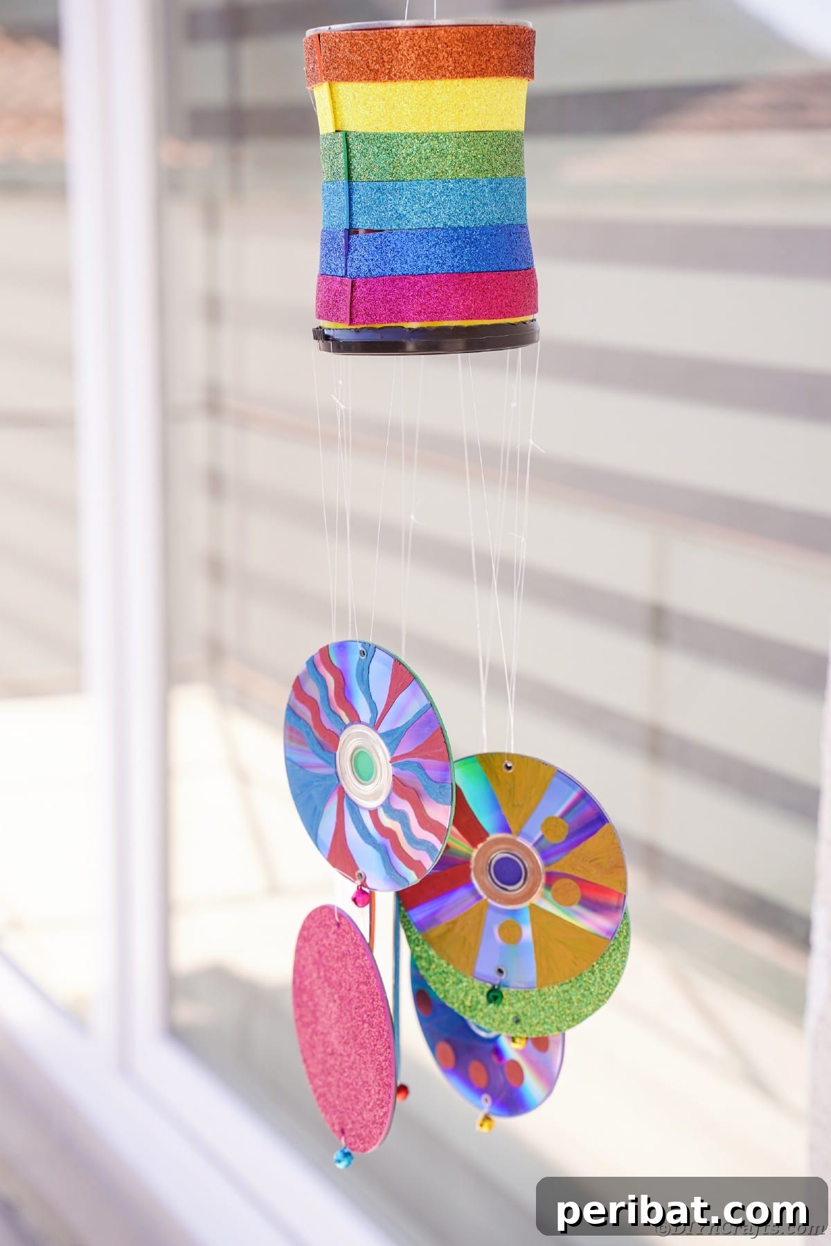 Sparkling Repurposed Garden Melody 23 A colorful wind chime hanging against a window with blinds, showing its vibrant reflection.