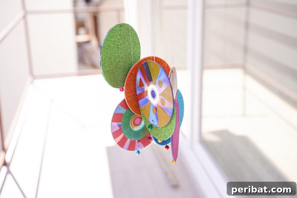 Sparkling Repurposed Garden Melody 4 The base of a CD wind chime, adorned with colorful elements, positioned near a window.