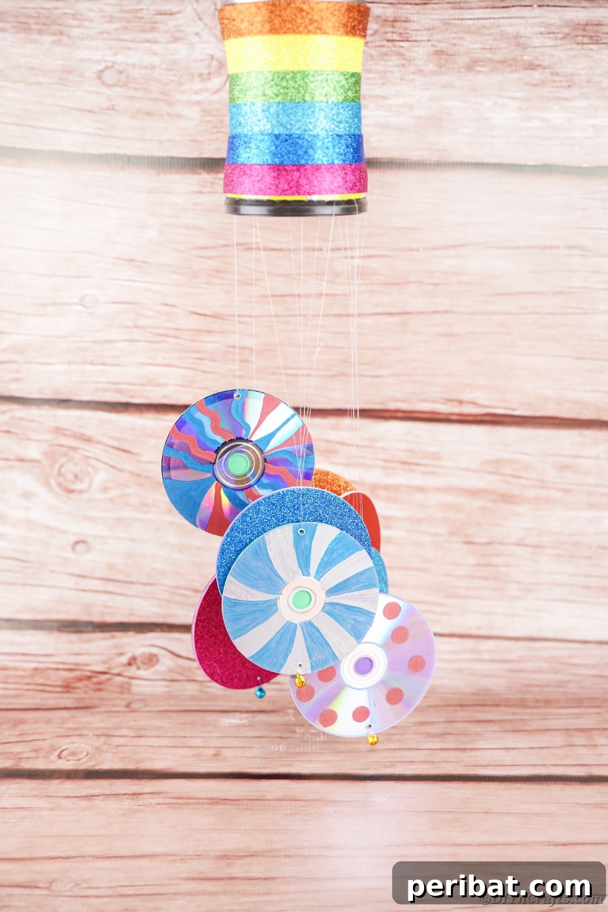Sparkling Repurposed Garden Melody 5 A colorful upcycled wind chime hangs gracefully against a rustic wooden wall, adding a touch of charm.