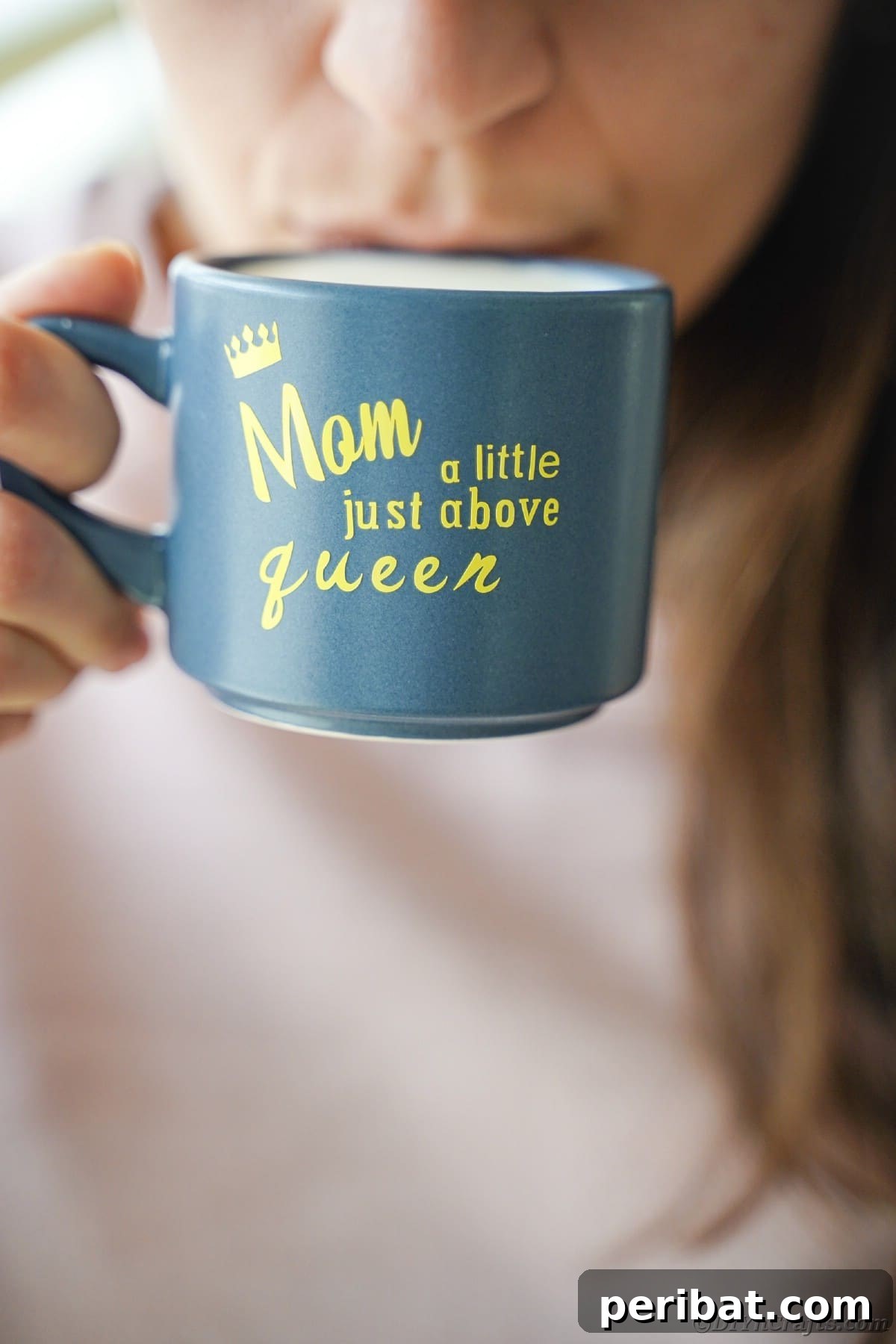 A woman's hand gently holding a vibrant blue mug with a cheerful yellow vinyl message, showcasing the completed DIY project.