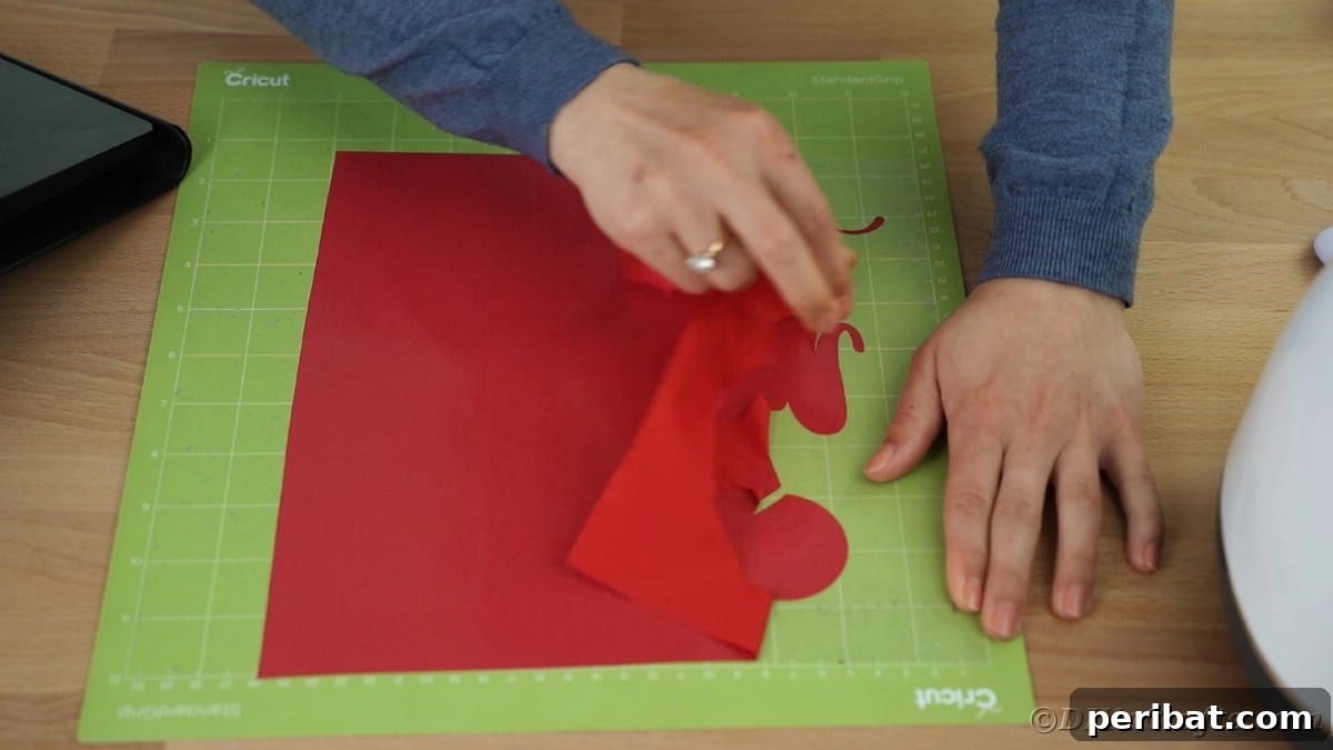 Hands carefully remove large pieces of excess heat transfer vinyl from around a cut message on a green Cricut mat.