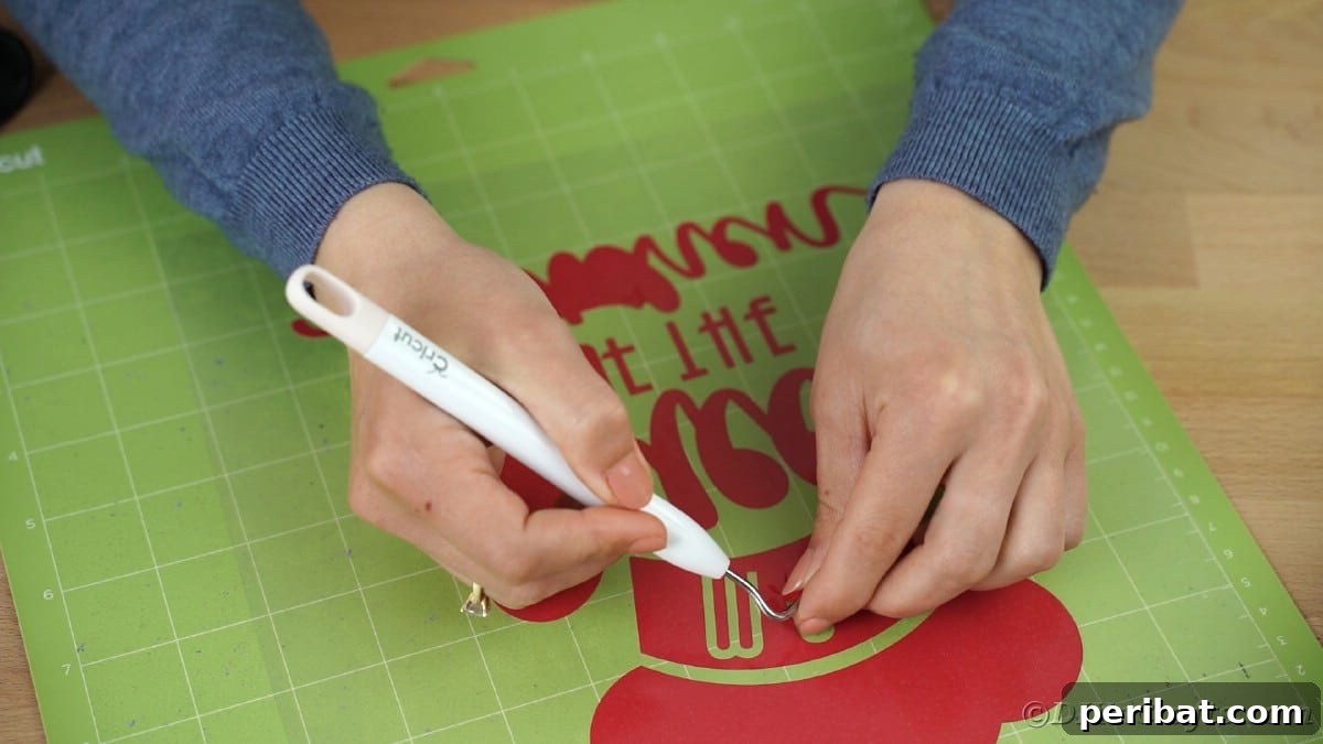 A weeding tool is used to meticulously remove small excess vinyl pieces from a red vinyl message, revealing the intricate design.