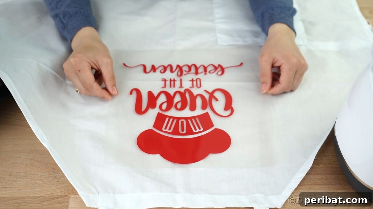 A hand carefully centers and places a vinyl design, attached to transfer tape, onto the front of a white apron.