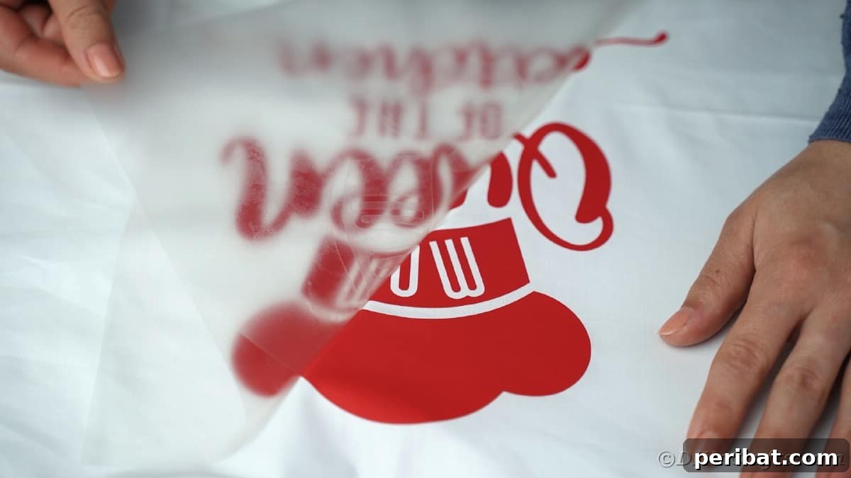 A hand gently peels a transparent transfer tape away from a newly applied vinyl message, revealing the design perfectly adhered to the apron.