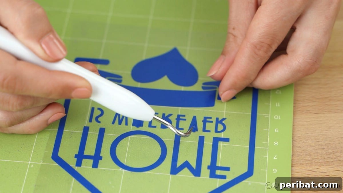 A weeding tool is used to remove small vinyl pieces from a blue message design, carefully positioned on a green Cricut mat.
