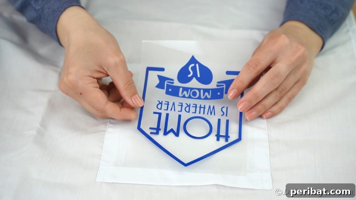 A hand carefully places a vinyl message onto the pocket of a white apron, ensuring precise positioning before heat application.