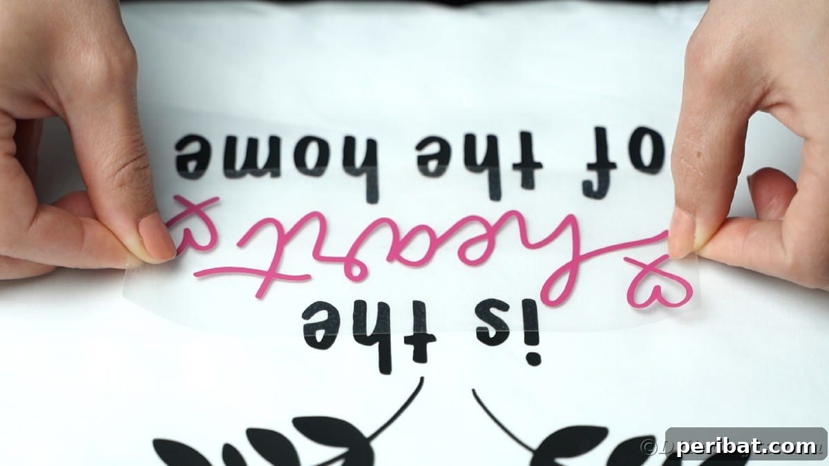 A hand carefully adds pink vinyl words onto a white apron, precisely layering them over a previously applied design.