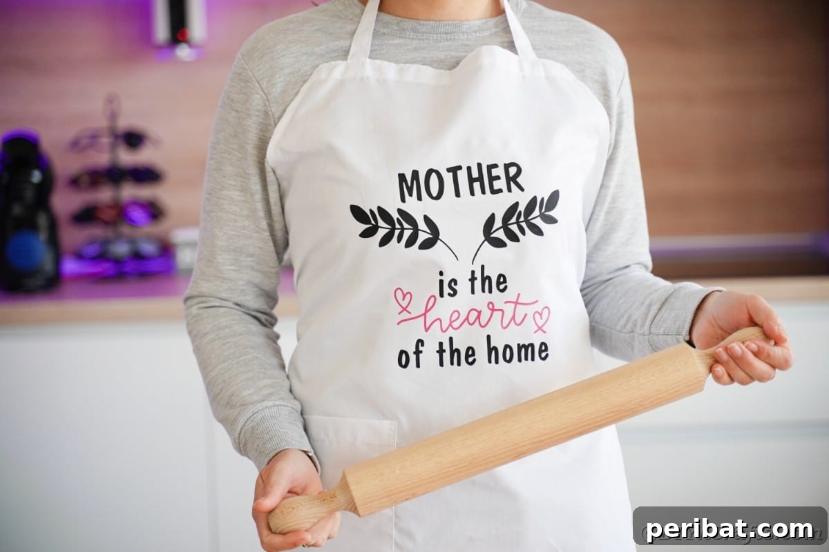 A woman in a crisp white apron, adorned with a custom Cricut vinyl design, smiles while holding a rolling pin, showcasing the personalized gift idea.
