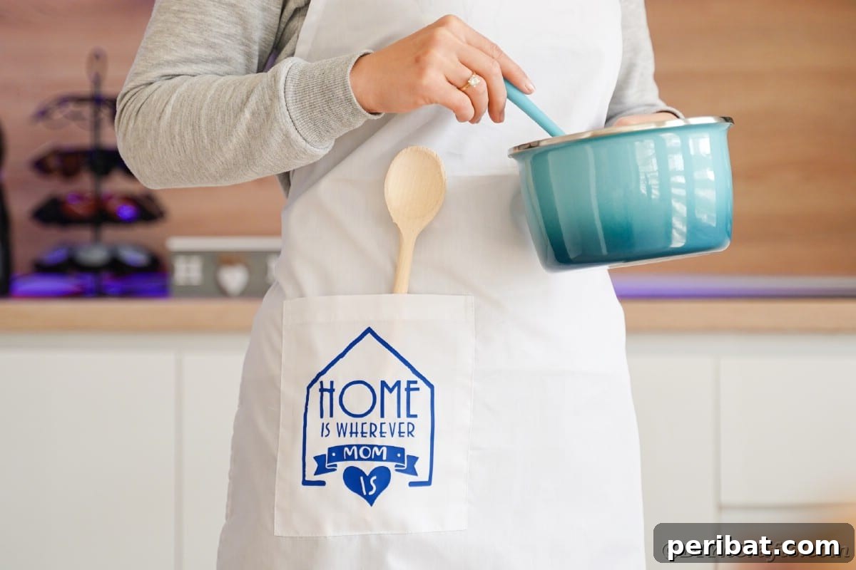 A crisp white apron features a custom blue Cricut vinyl message on its pocket, showcasing a neat and personalized detail, ready for kitchen use.