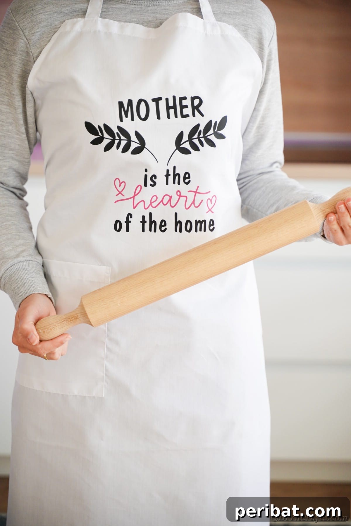A woman wears a white apron with a black vinyl message across the front, holding a rolling pin, emphasizing the personalized aspect of the gift.
