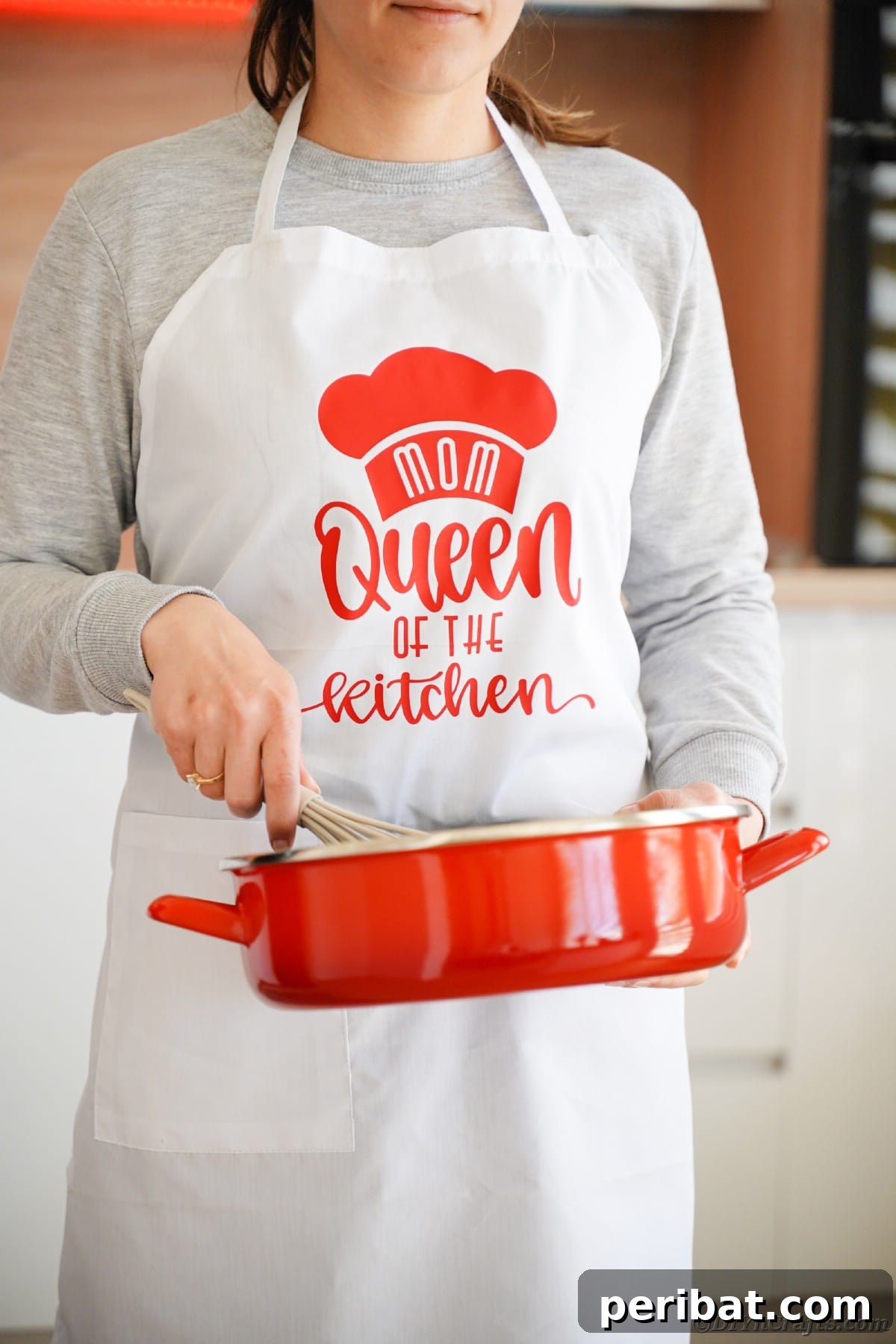 A woman in a personalized apron enthusiastically stirs a red skillet, embodying the joy of cooking in a custom kitchen garment.