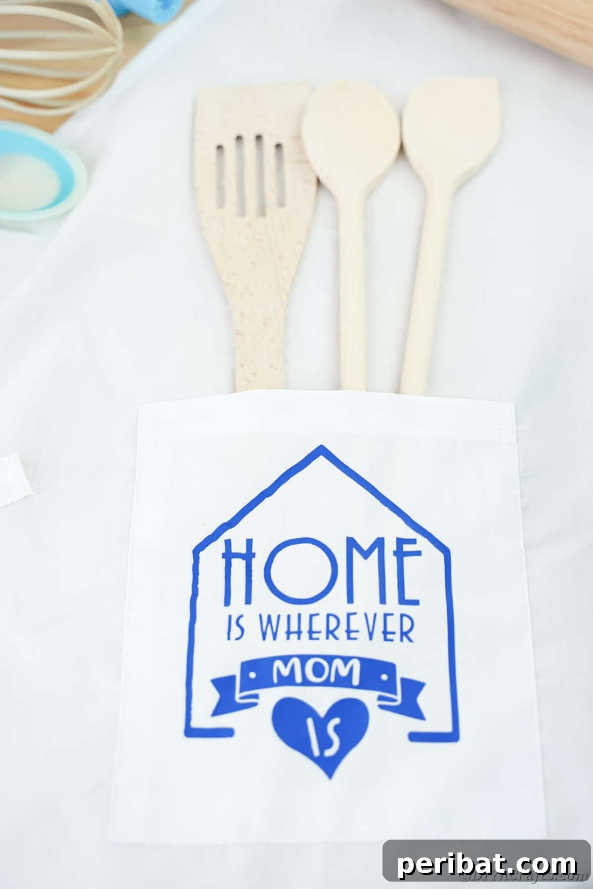 A close-up of a white fabric surface featuring the blue vinyl message 'Home is wherever Mom is', highlighting a heartfelt custom design.