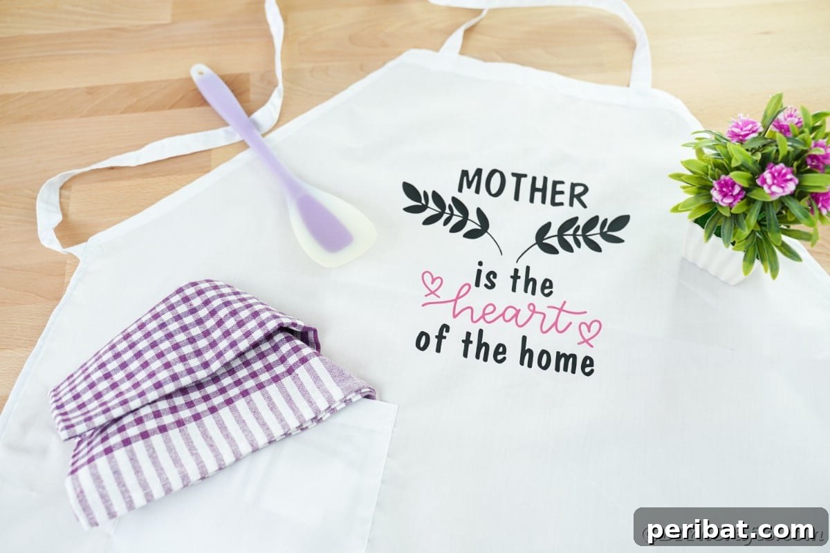 A close-up view of a white apron adorned with a black and pink Cricut vinyl message, displayed neatly on a table, showcasing a vibrant design.
